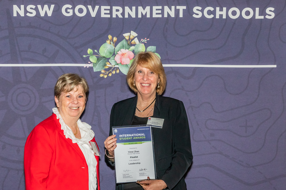 Two women standing in front of a purple screen, one holding a certificate